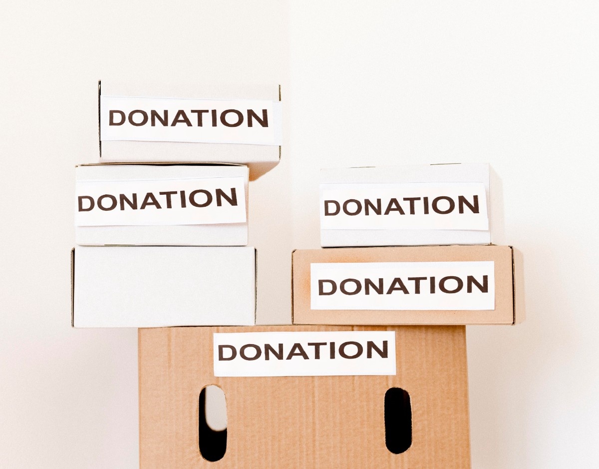 Two smiling girls holding cardboard recycling boxes standing next to a whiteboard with a colored recycling symbol and words glass, plastic, and paper.