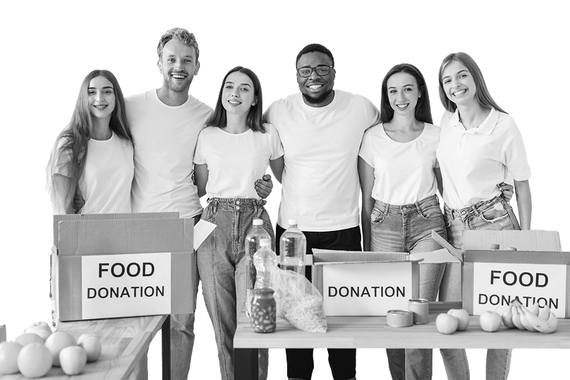 Group of six smiling volunteers standing behind tables with boxes labeled 'Food Donation' and various food items.